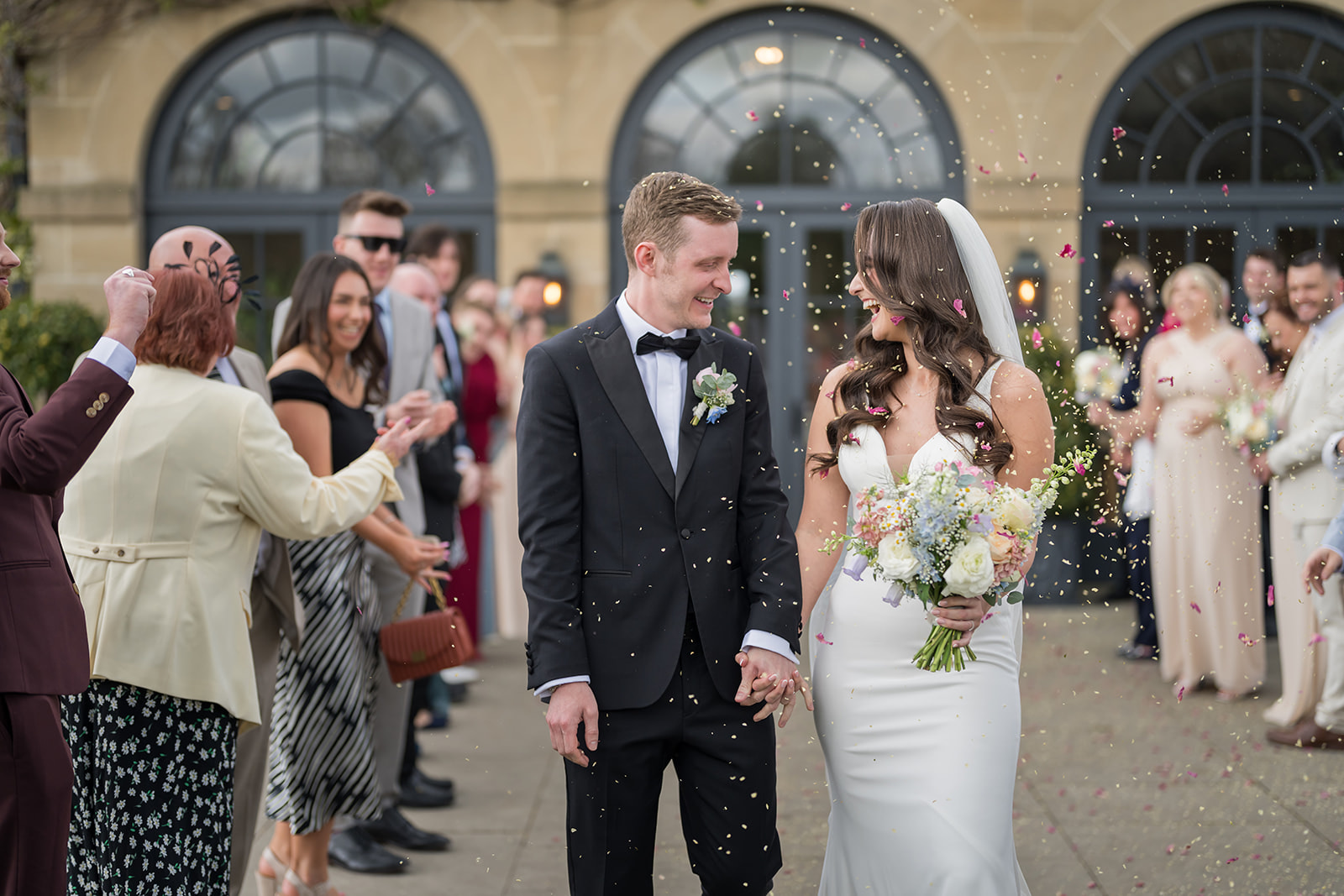 Becky and Alex smiling as guests throw confetti at Middleton Lodge
