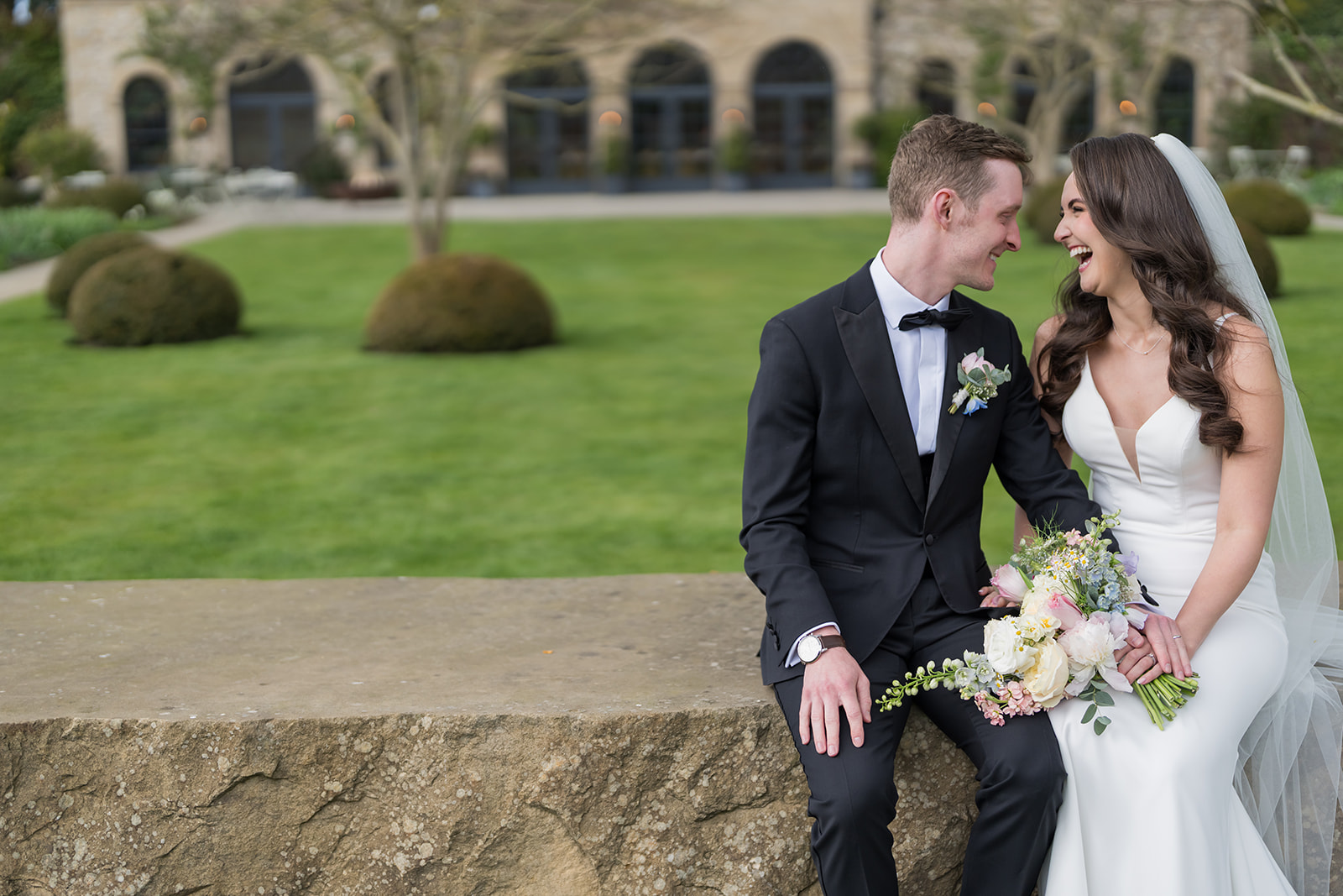 Becky and Alex sitting together on a stone wall in Middleton Lodge’s gardens