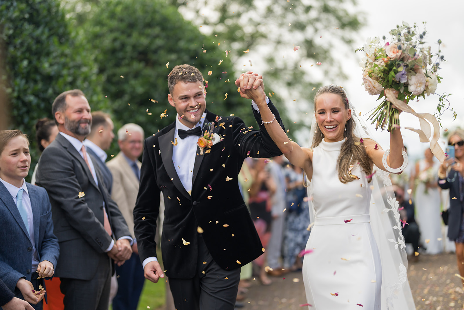 Bex and Christian raising their hands beneath confetti outside St Peter’s Church in Heswall