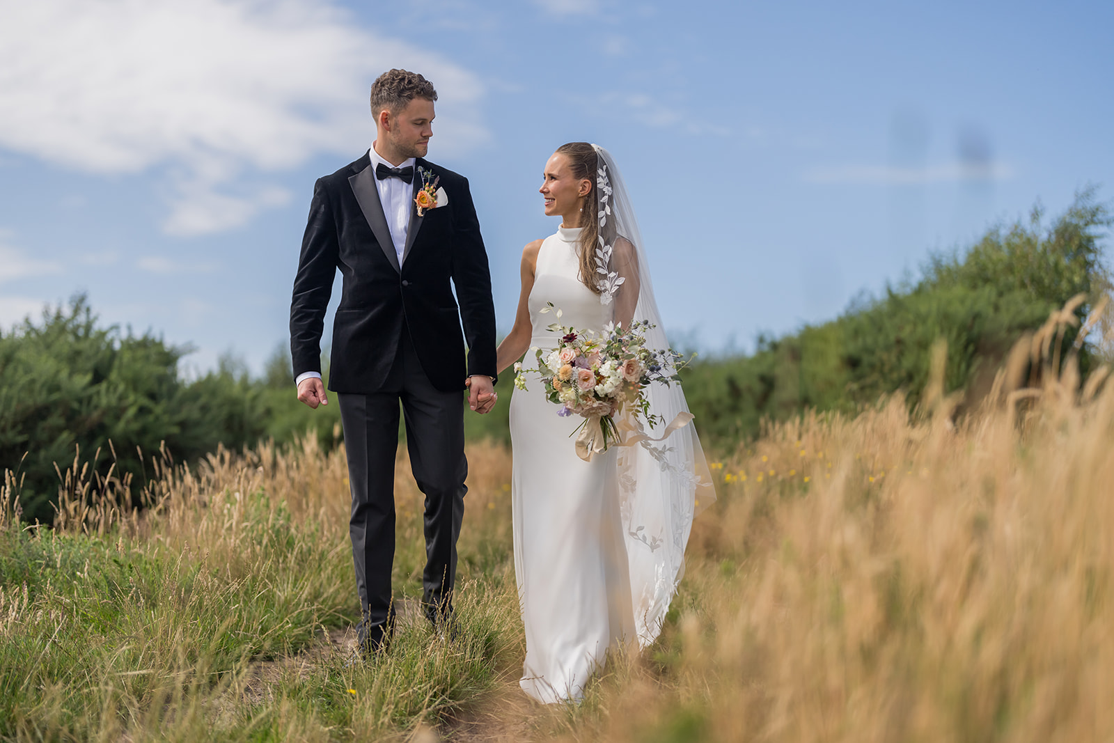 Bex and Christian holding hands while walking through tall grass in Wirral