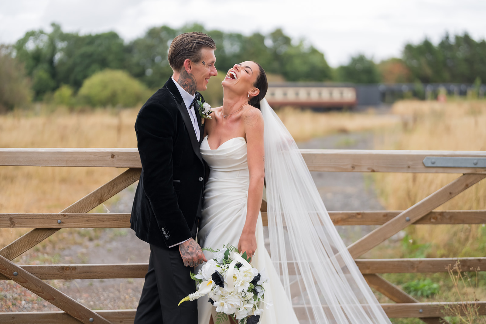Ellie and Thomas laughing together beside the wooden gate at Whistle Barns
