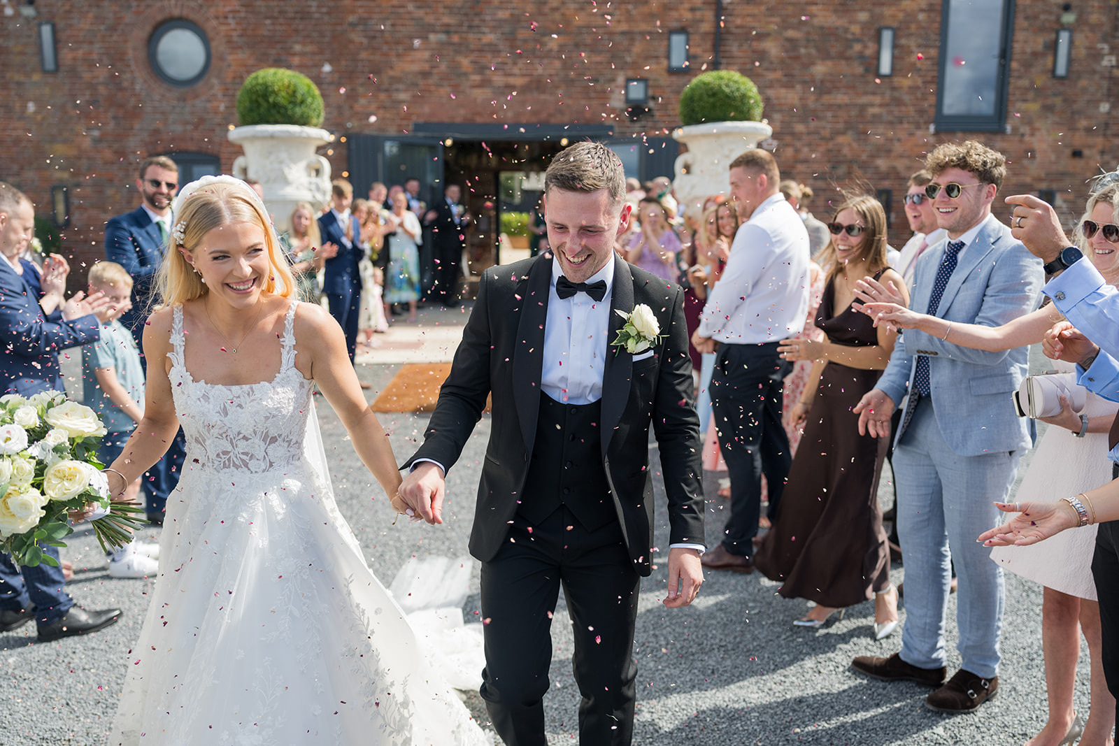 Evie and Josh walking through confetti outside Burlton Manor