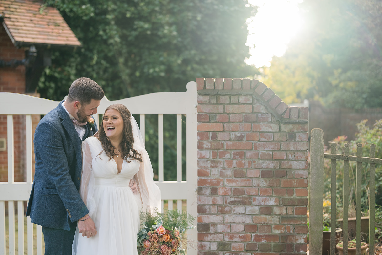 Gemma and James laughing beside the brick garden entrance at Abbeywood Estate
