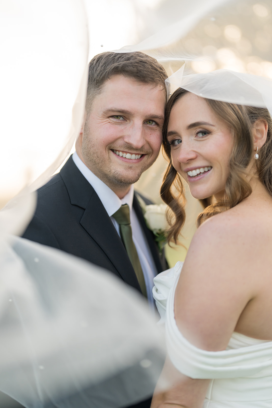 Harriet and Gareth smiling together beneath her veil at Hyde Bank Farm