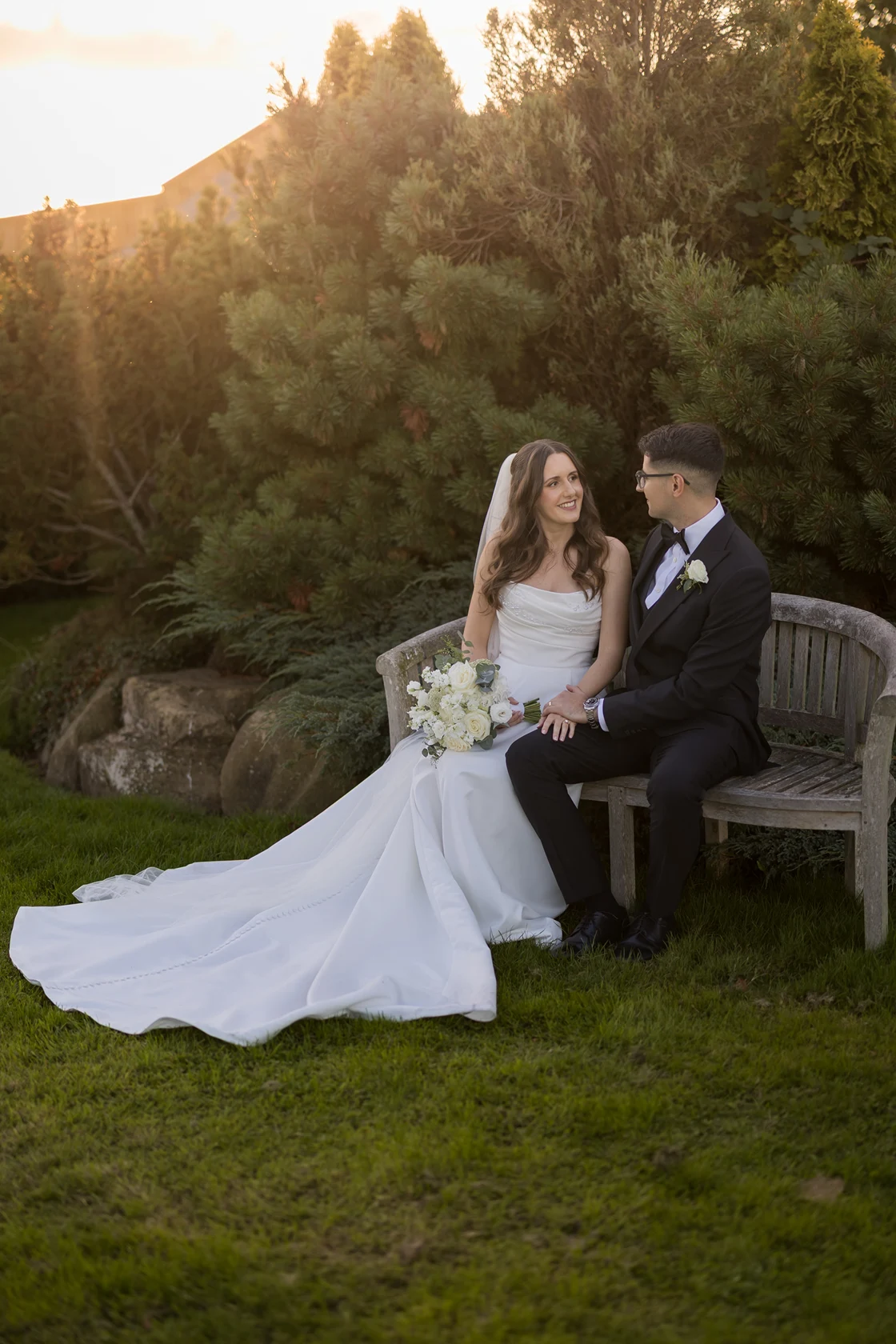 Katja and Huseyin sitting together on a garden bench in evening light at Sandhole Oak Barn