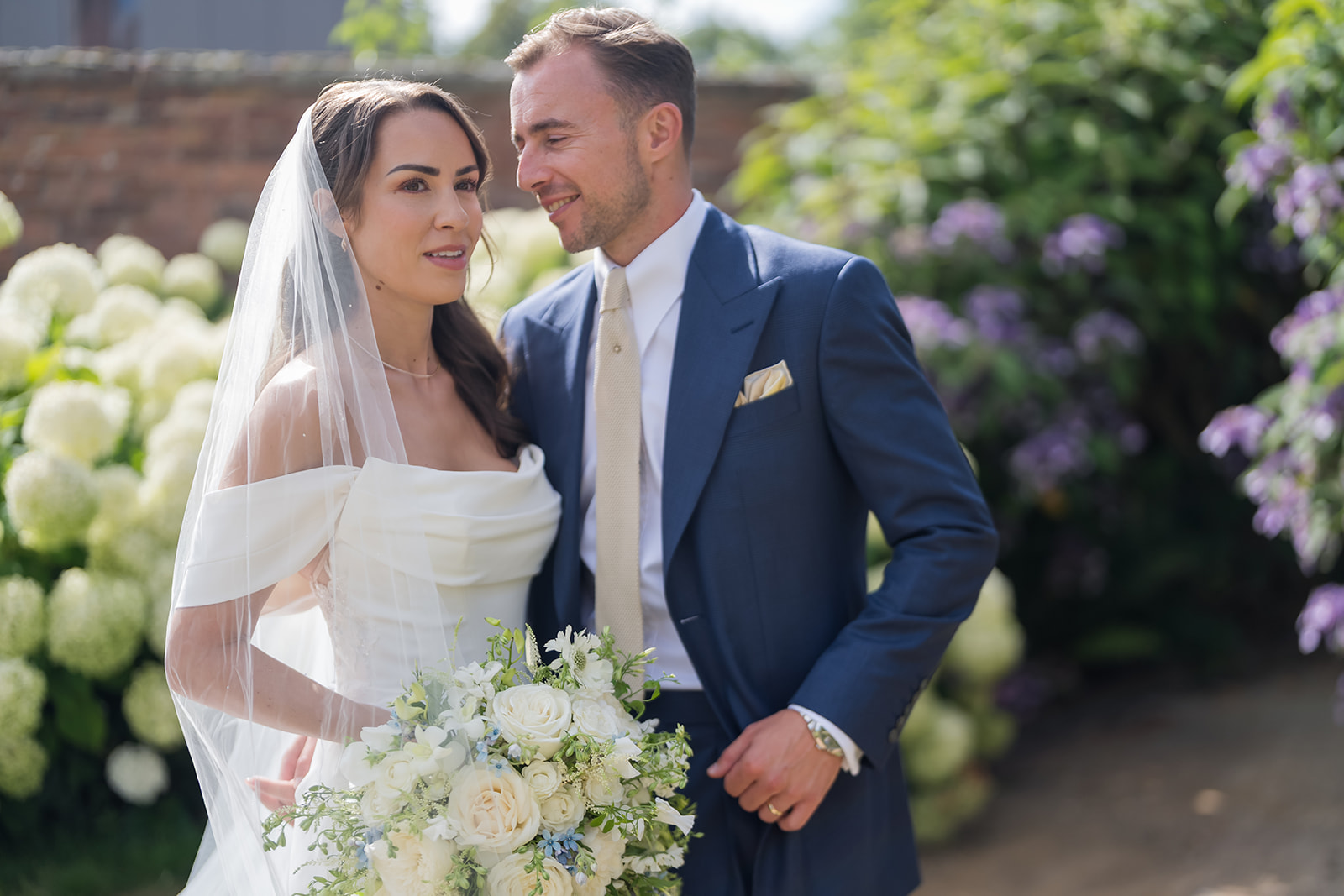 Lizzie holding her white bouquet beside Jack in the gardens at Dorfold Hall