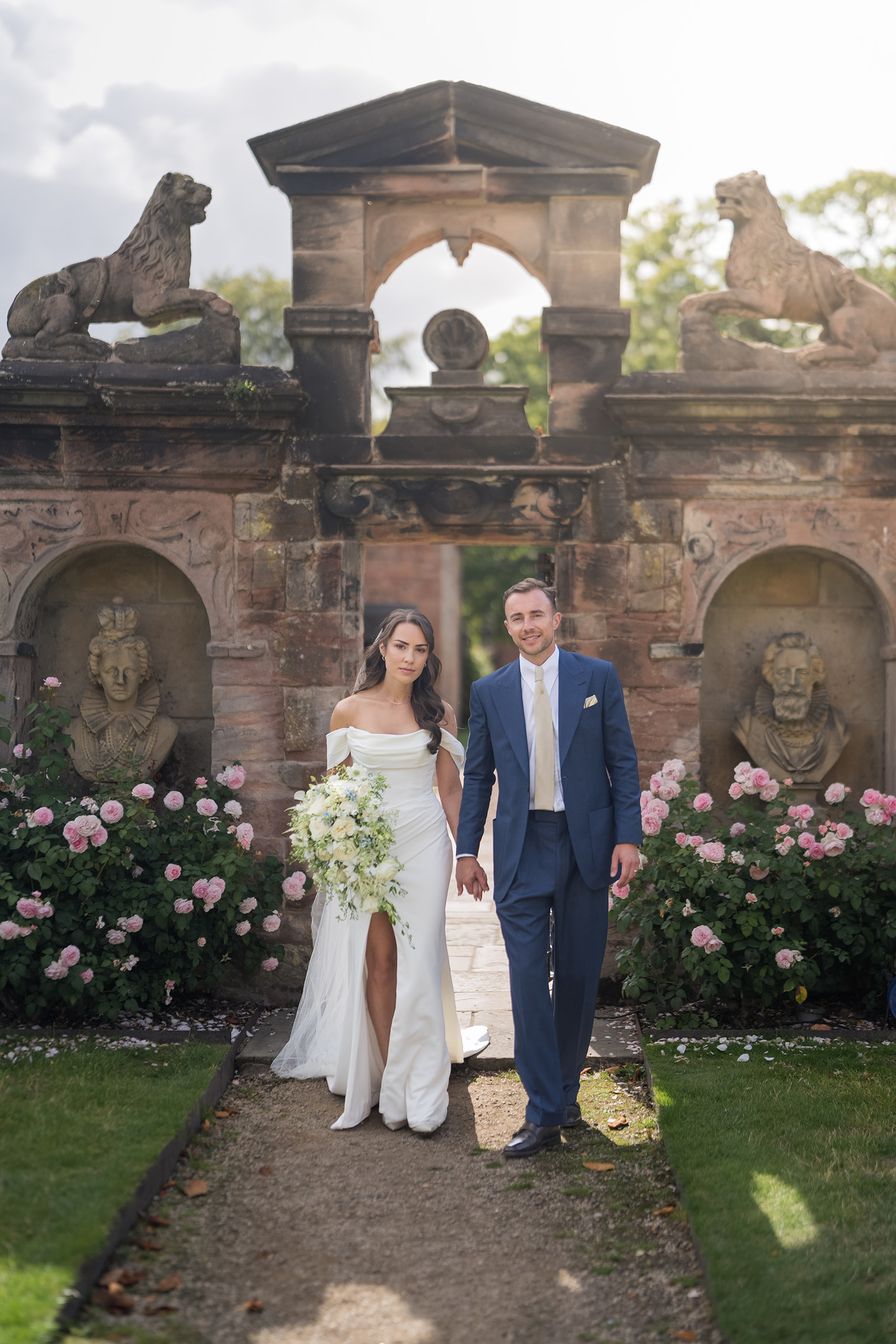 Lizzie and Jack holding hands beneath the stone garden arch at Dorfold Hall