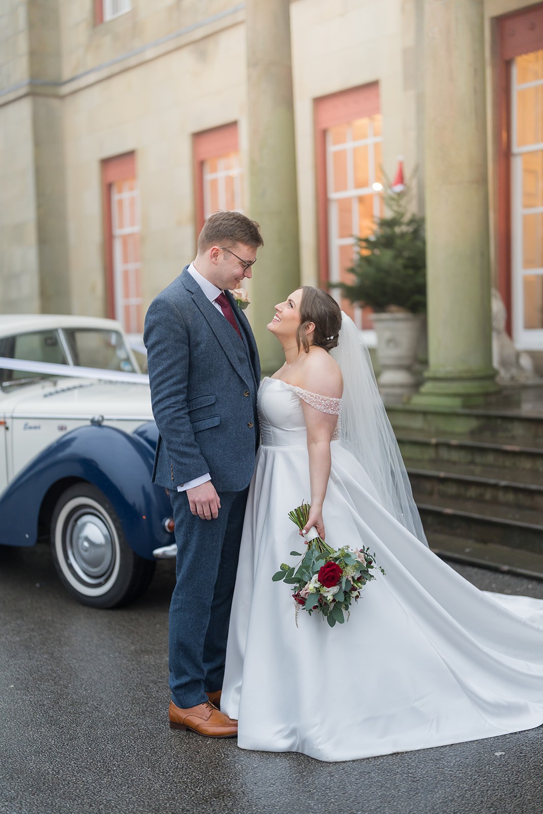 Bride and groom beside a vintage car outside a country house
