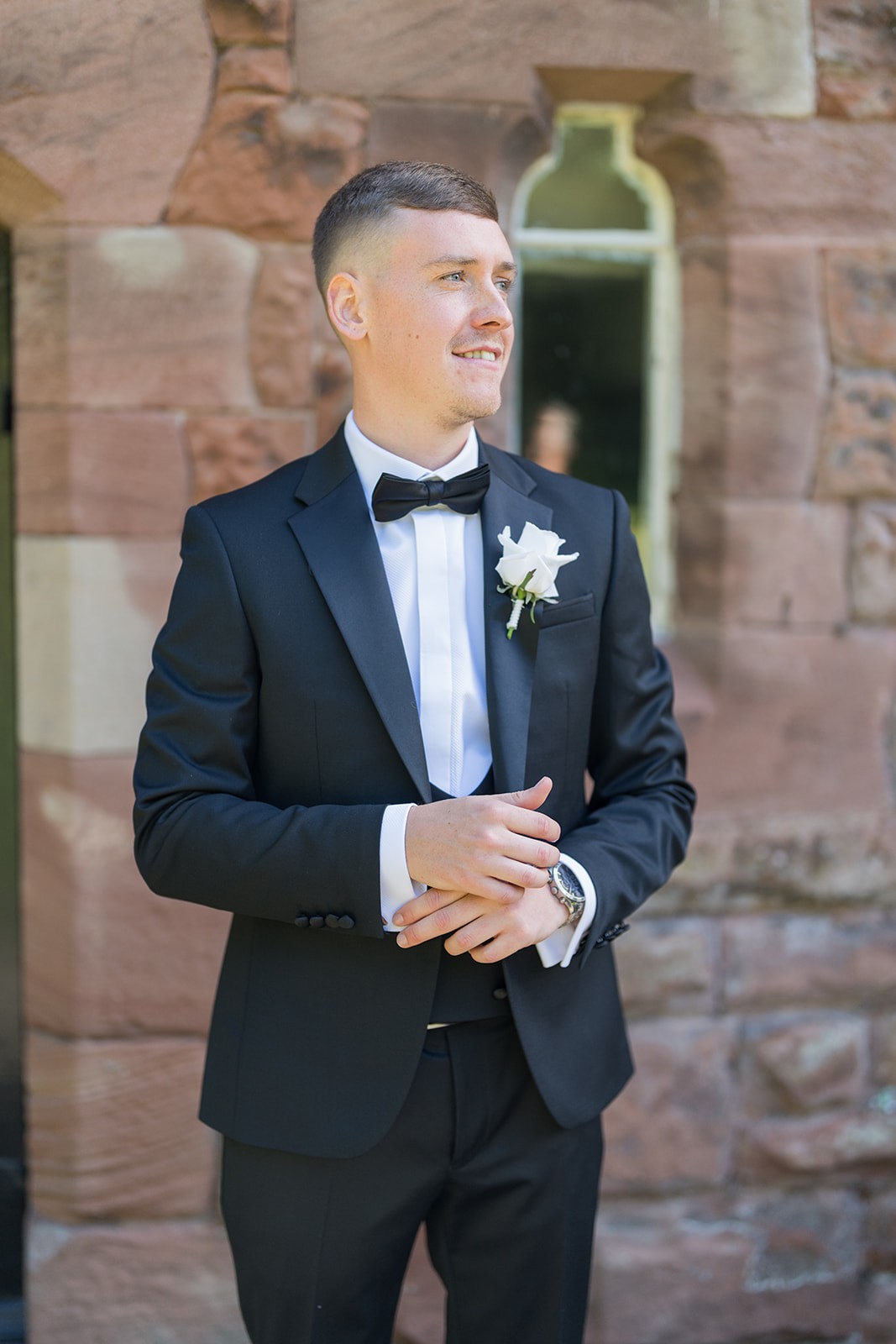 Groom adjusting his cuff outside a brick building