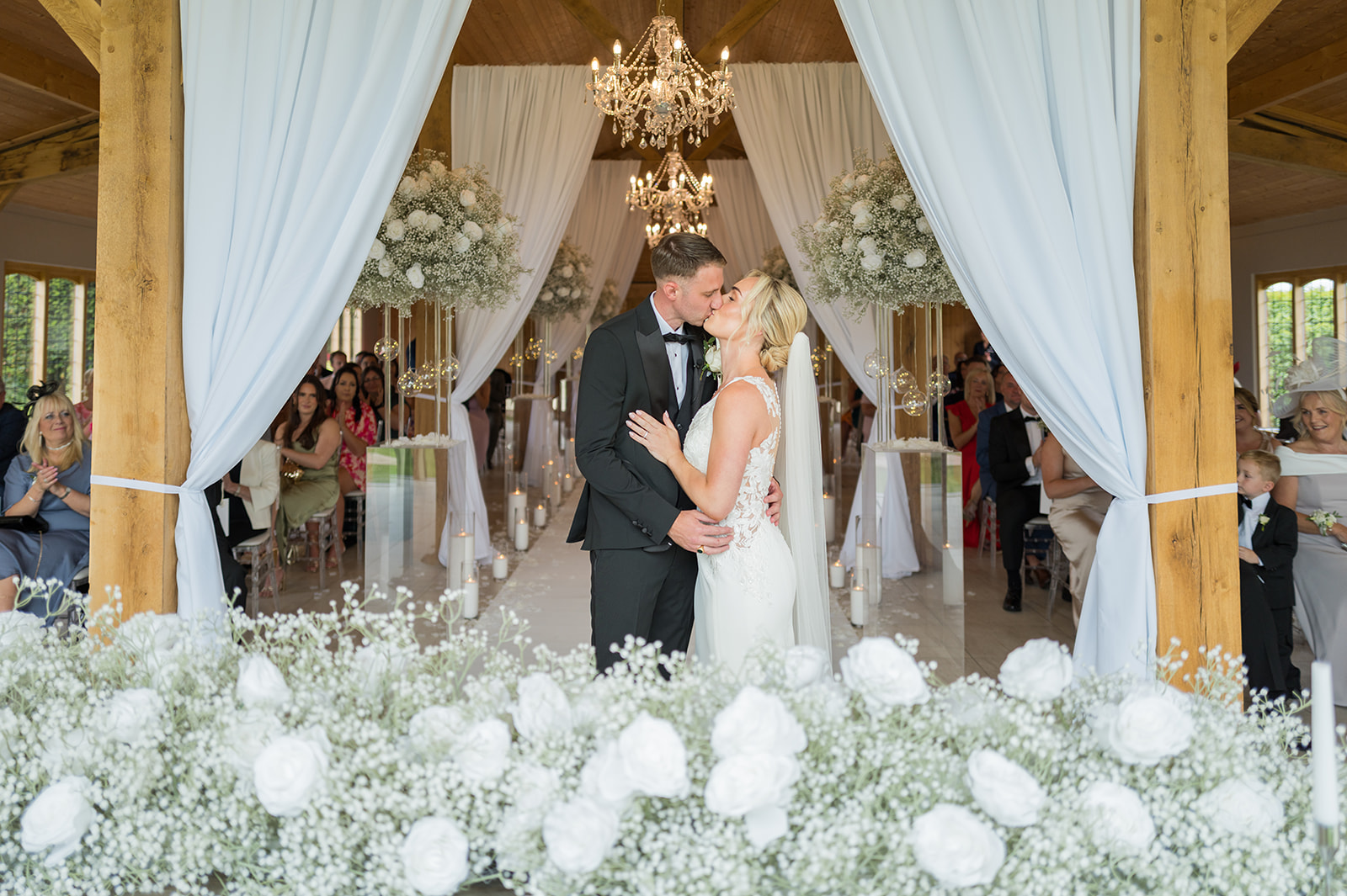 Newlyweds kissing beneath draped curtains and a white floral arch