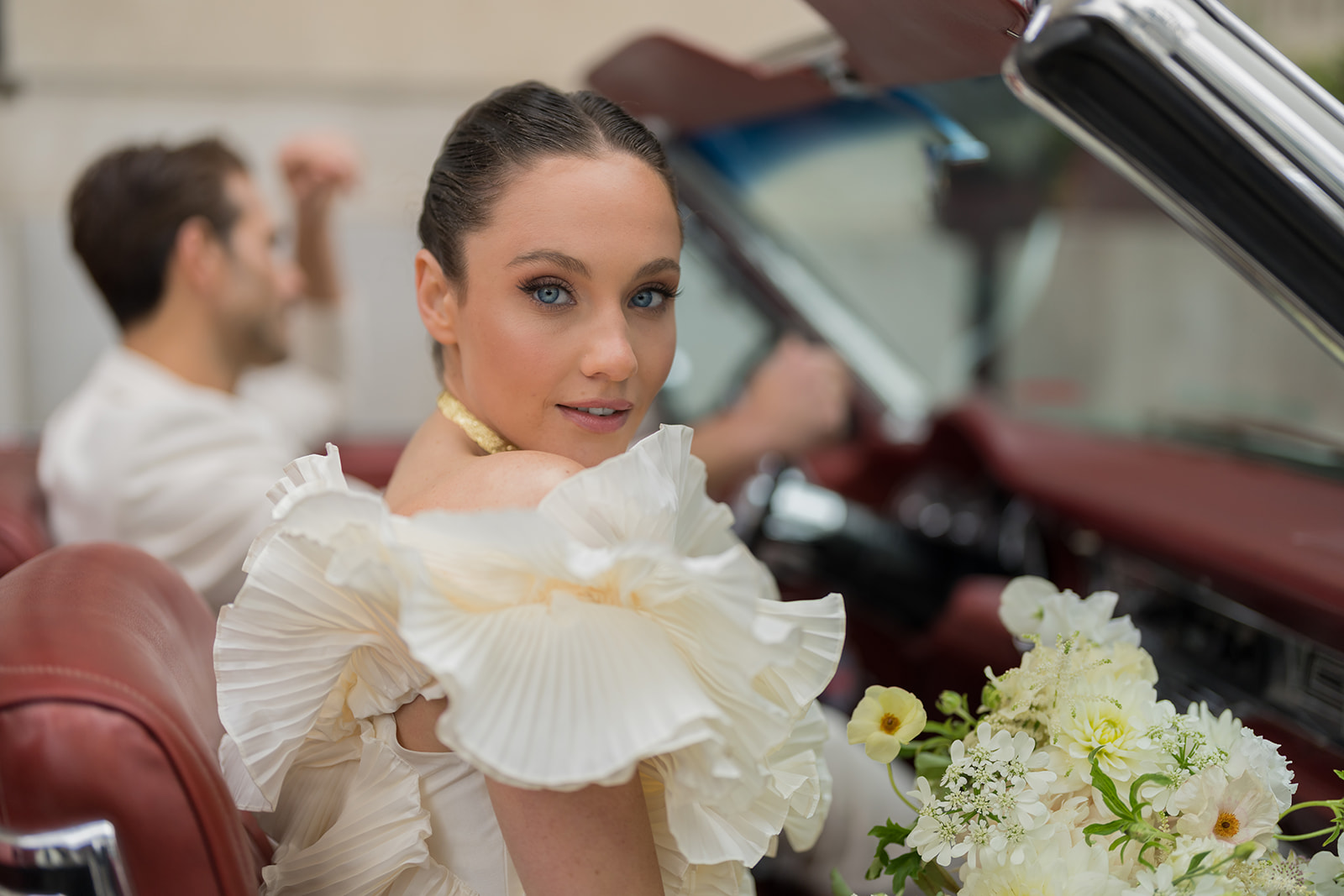 Bride seated in a wedding car holding white flowers