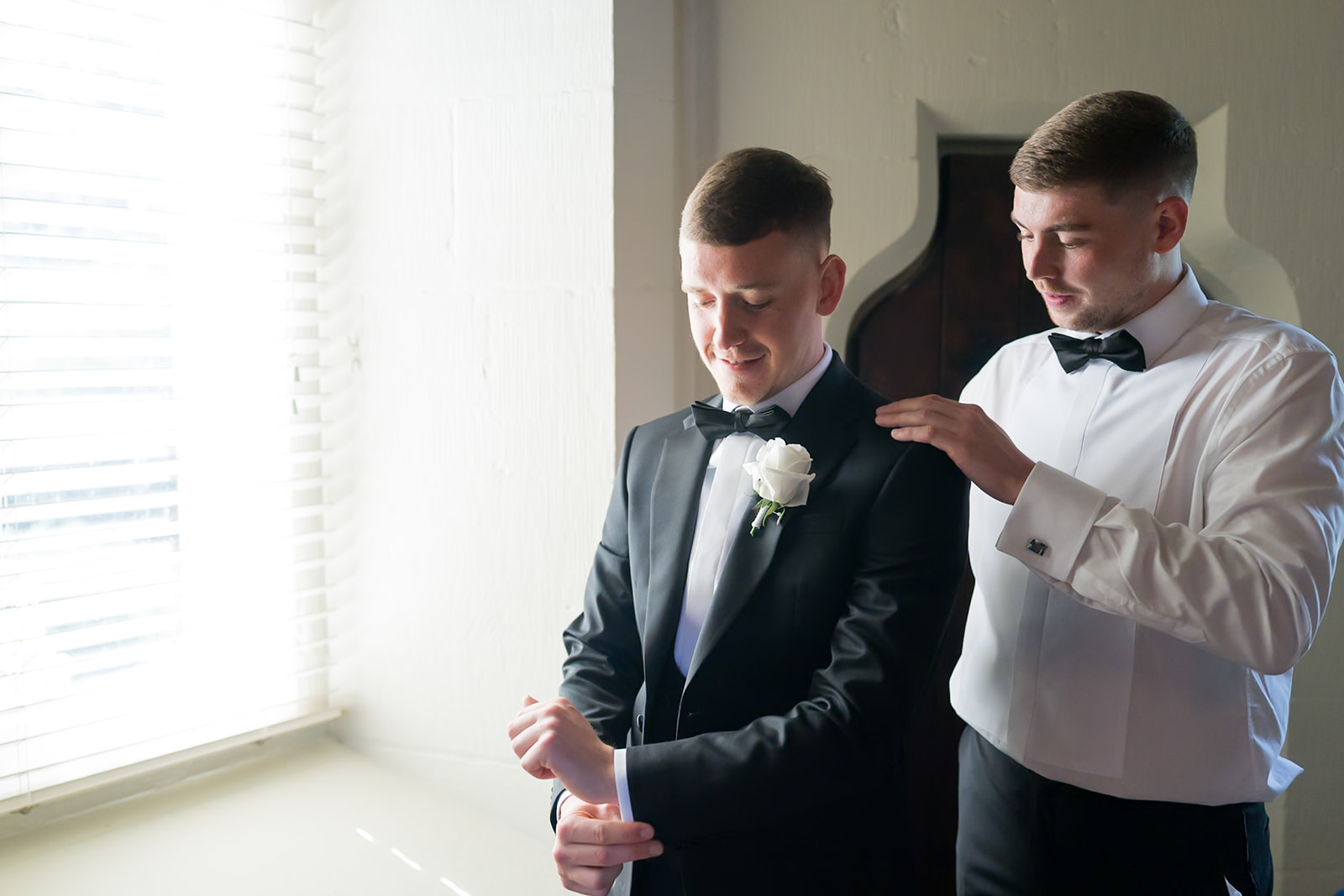 Groom having his bow tie adjusted beside a bright window