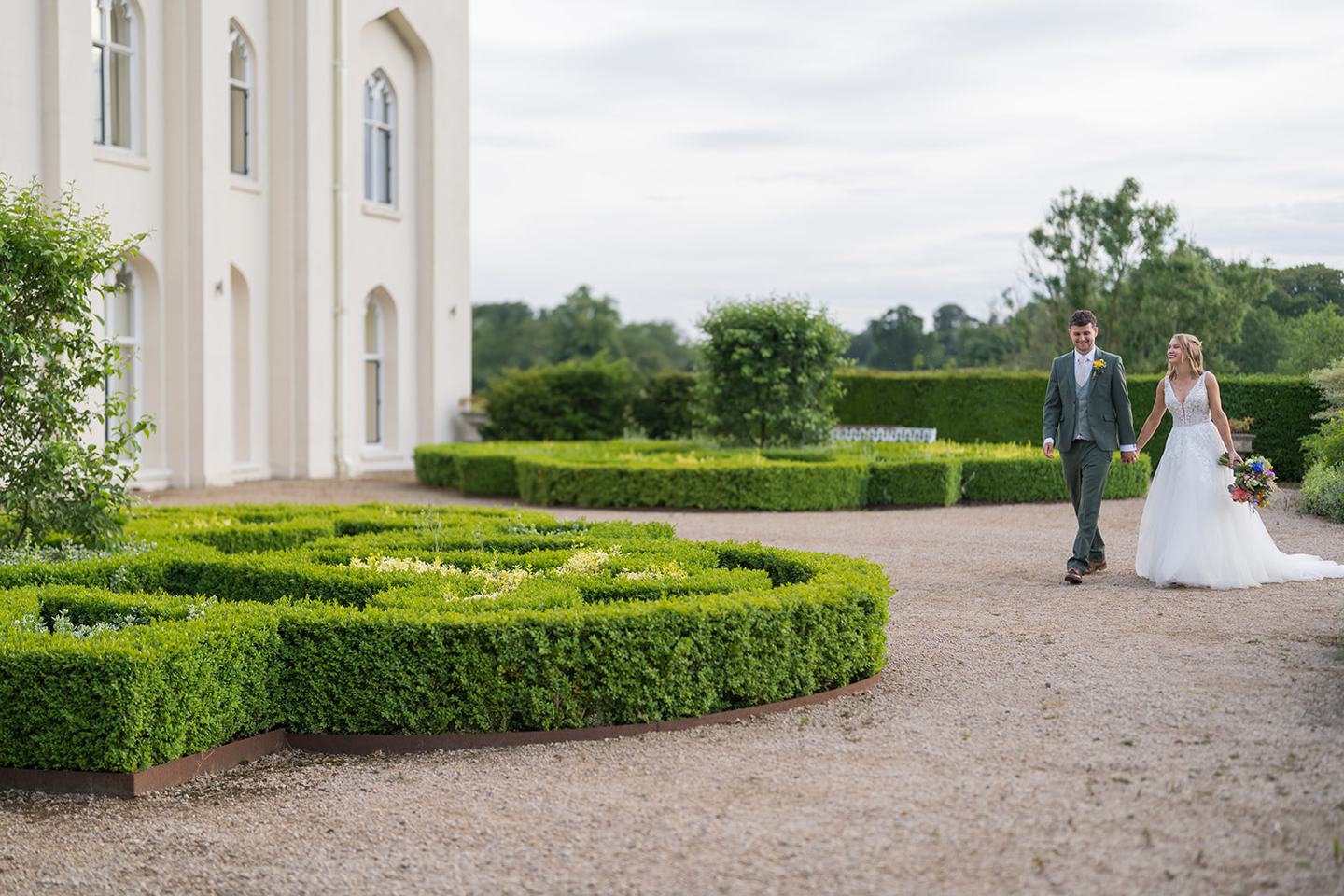 Newlyweds walking beside the Abbey at Hannah and Jacob’s Combermere Abbey wedding