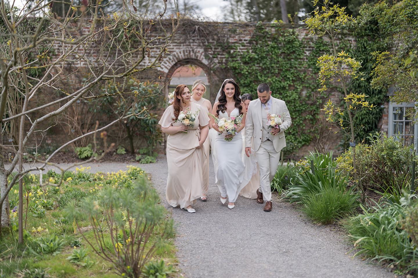 Bridal party walking through the gardens at Becky and Alex’s Middleton Lodge wedding
