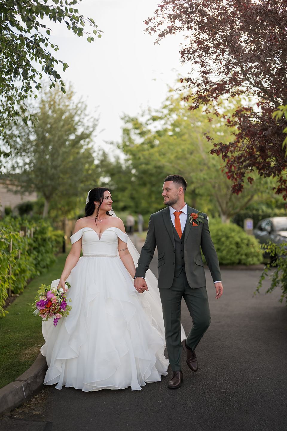 Newlyweds walking through the gardens at Kate and Kieran’s Mythe Barn wedding